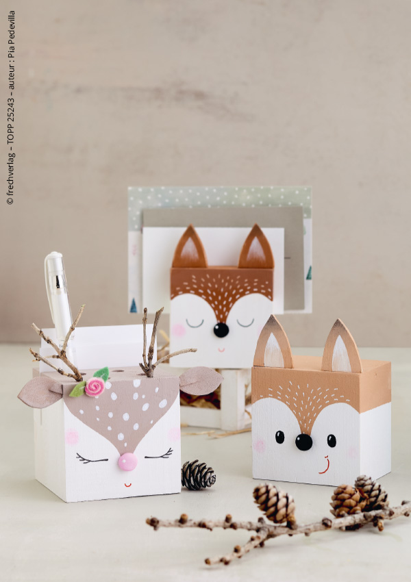 Trois pots à crayons en bois en forme de tête d'animaux (renard et biche), décorés avec des bois en brindilles et des fleurs en feutrine, entourés de pommes de pin